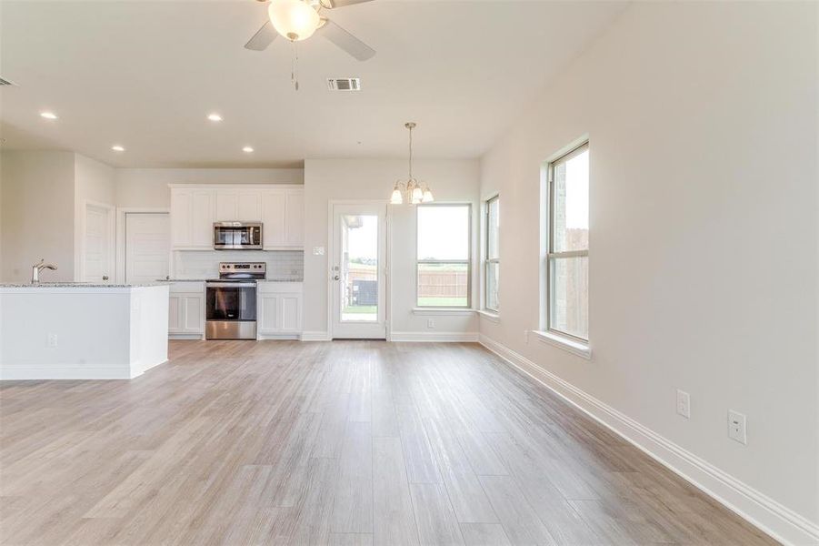 Unfurnished living room featuring ceiling fan with notable chandelier and light hardwood / wood-style floors