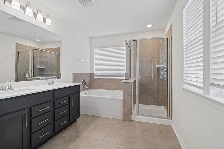 This primary bathroom is definitely move-in ready! Featuring an oversized tub and walk-in shower with tile surround, stained cabinets with light countertops, dual vanities, high ceilings, neutral paint, sleek and modern finishes.