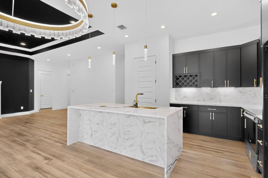 A sophisticated kitchen boasts a grand marble waterfall island, complemented by sleek black cabinetry and wood flooring.