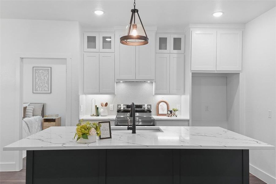 Spacious kitchen featuring a large island with a stone-finish countertop, white upper cabinetry with glass-front accents, dark lower cabinetry, and recessed lighting Spacious kitchen featuring a large island with a stone-finish countertop, white upper cabinetry with glass-front accents, dark lower cabinetry, and recessed lighting