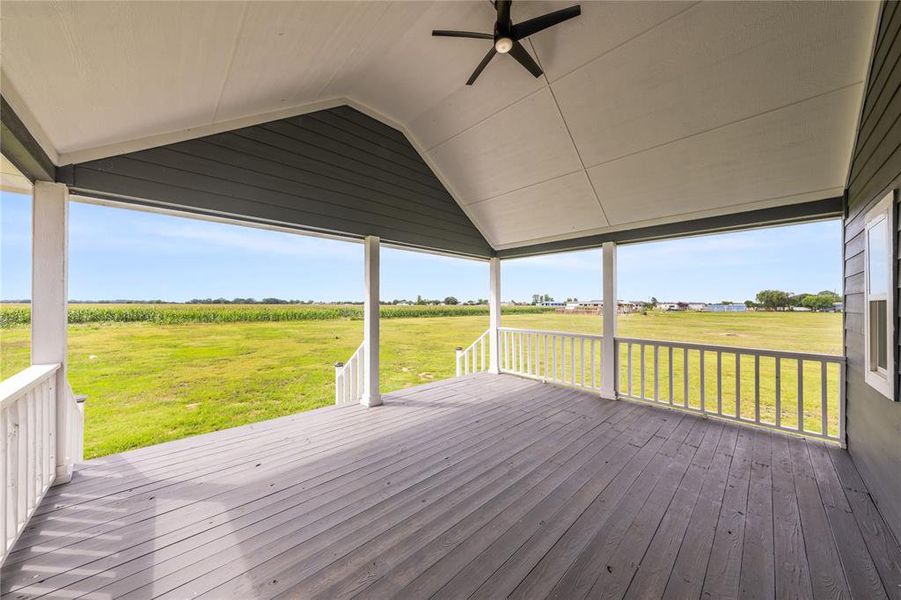 Expansive covered porch featuring a painted wood-finish deck, white railing, and a vaulted ceiling with a ceiling fan