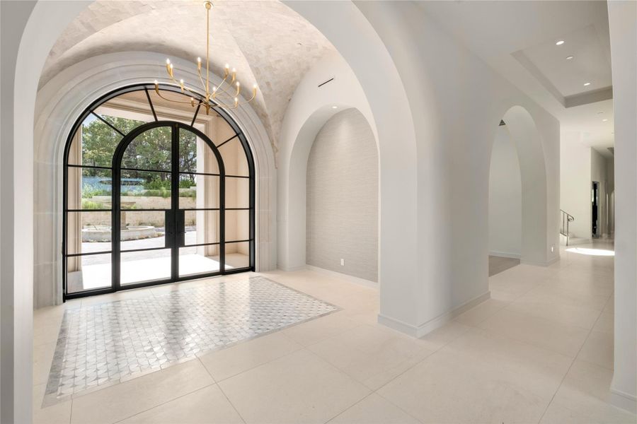 Foyer features tiled groin vaulted ceiling and mosaic rug with tall niches.