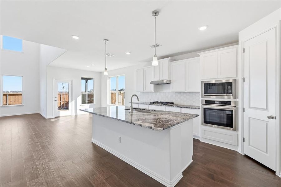 Modern kitchen featuring a large island with a stone countertop, white shaker-style cabinetry, stainless steel appliances, and wood-finish flooring