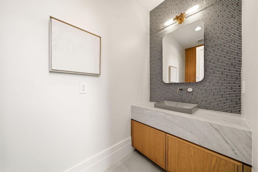 First floor stylish powder bath with floating-style marble vanity, designer lighting, and mosaic accent wall. First floor stylish powder bath with floating-style marble vanity, designer lighting, and mosaic accent wall.