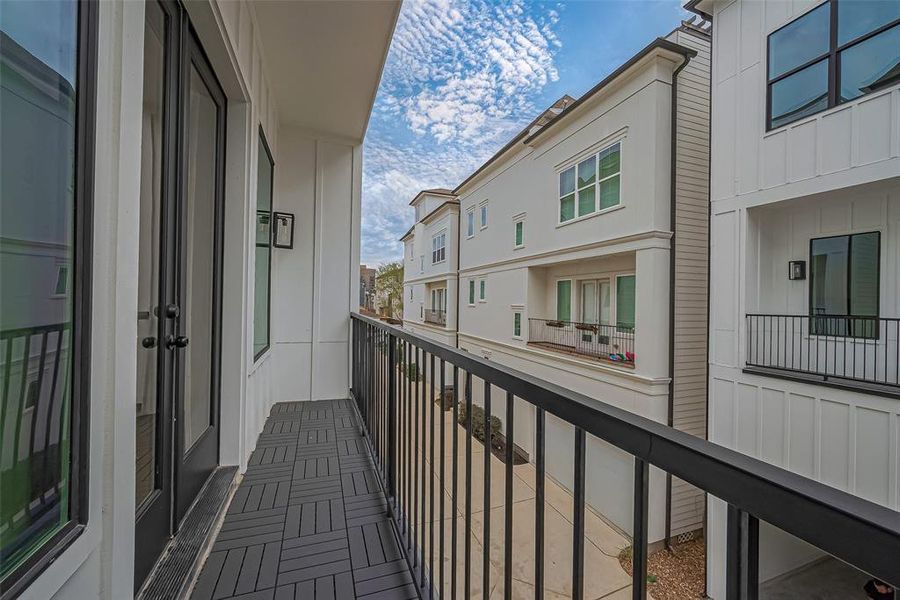 This photo showcases a modern balcony with sleek black railings and flooring, offering a view of neighboring townhouses and a bright, partly cloudy sky.