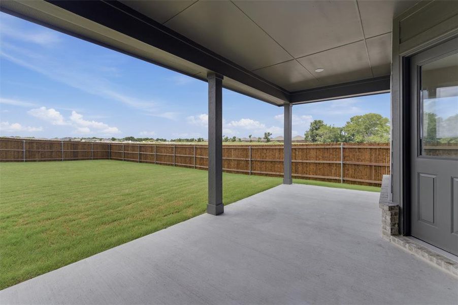 Covered concrete patio with recessed lighting, offering direct access to a fenced backyard featuring a manicured lawn and wood privacy fencing Covered concrete patio with recessed lighting, offering direct access to a fenced backyard featuring a manicured lawn and wood privacy fencing