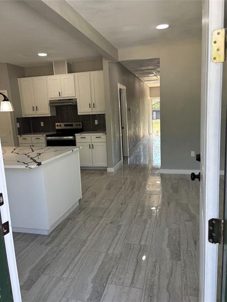 Kitchen with backsplash, white cabinets, range, exhaust hood, and recessed lighting Kitchen with backsplash, white cabinets, range, exhaust hood, and recessed lighting