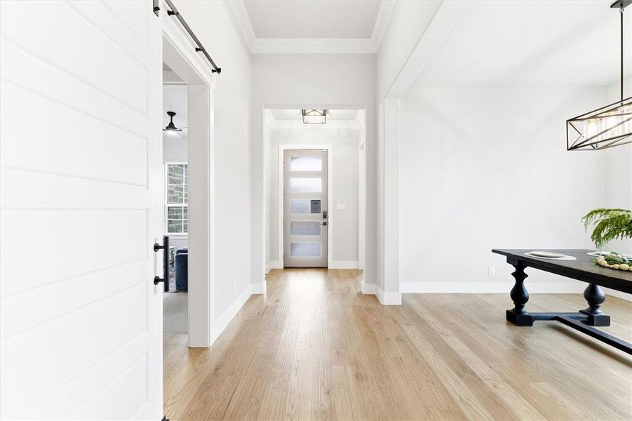 Hallway with a barn door, ornamental molding, and light wood finished floors