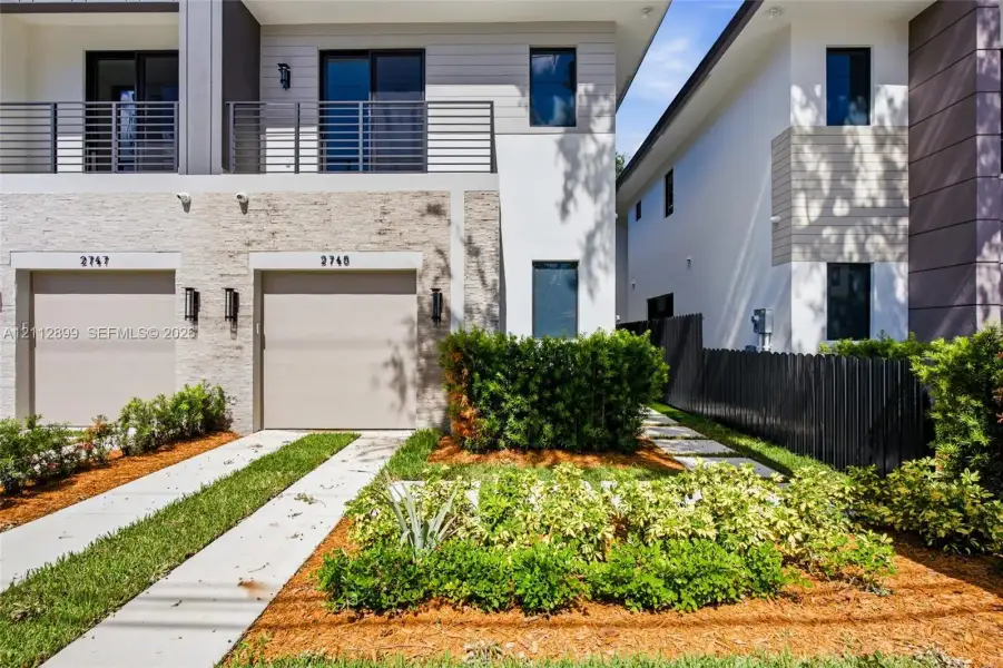 Modern exterior featuring stone veneer siding, a second-story balcony with metal railings, horizontal lap siding, and a concrete driveway with a central grass strip