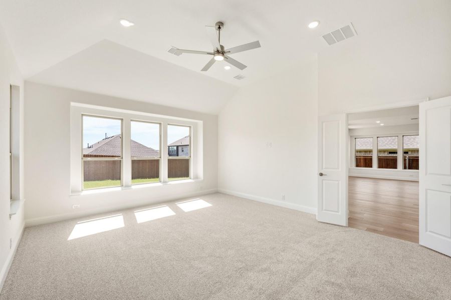 Empty bedroom with vaulted ceiling, ceiling fan, carpet flooring, and triple windows overlooking backyard Empty bedroom with vaulted ceiling, ceiling fan, carpet flooring, and triple windows overlooking backyard