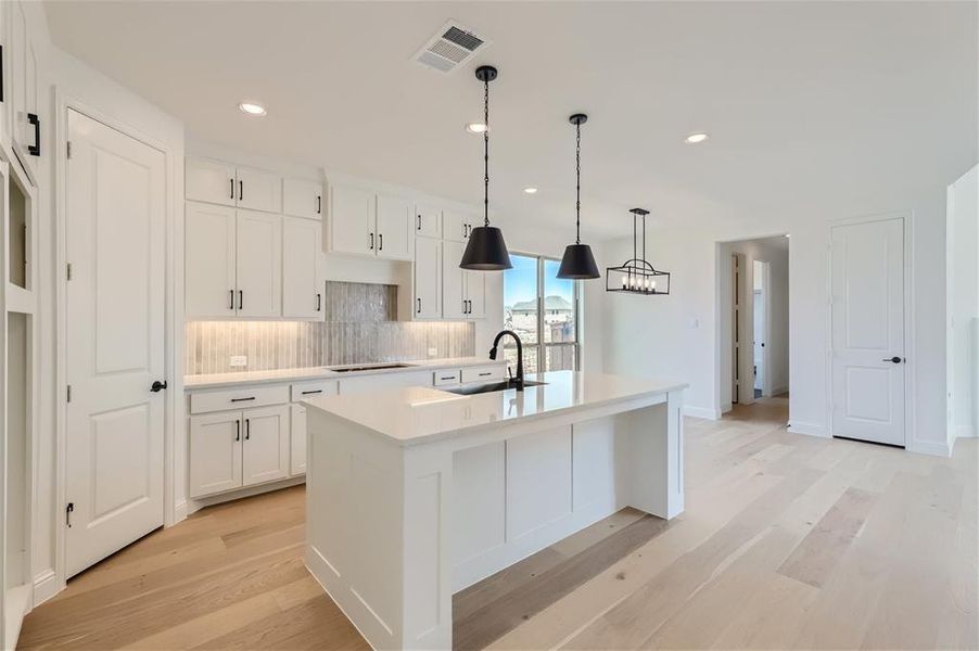 Kitchen with tasteful backsplash, a center island with sink, light wood-type flooring, sink, and white cabinets