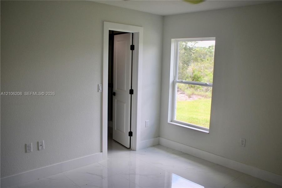 Neutral-toned interior room featuring large-format tile flooring, a single-hung window with natural lighting, and a solid-core interior door with matte black hardware
