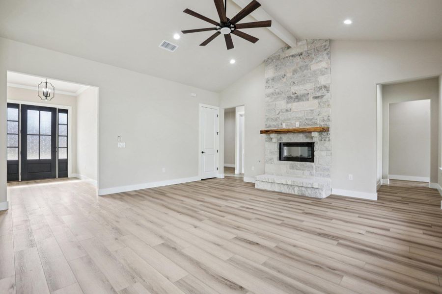 Unfurnished living room featuring beamed ceiling, light wood-style floors, ceiling fan, a stone fireplace, and high vaulted ceiling