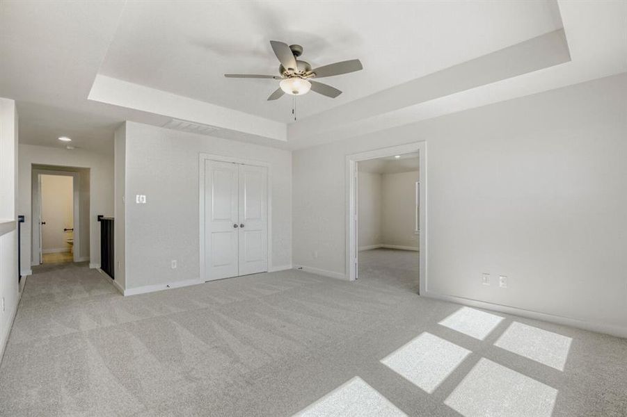 Unfurnished bedroom featuring a tray ceiling, light colored carpet, a closet, and a ceiling fan