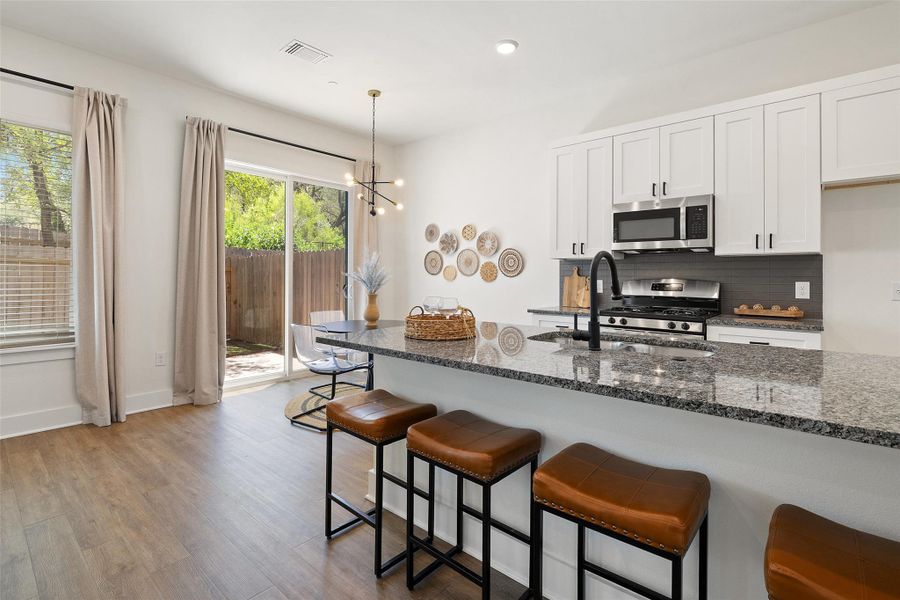 Kitchen featuring wood finished floors, appliances with stainless steel finishes, white cabinets, dark stone counters, and a breakfast bar area Kitchen featuring wood finished floors, appliances with stainless steel finishes, white cabinets, dark stone counters, and a breakfast bar area