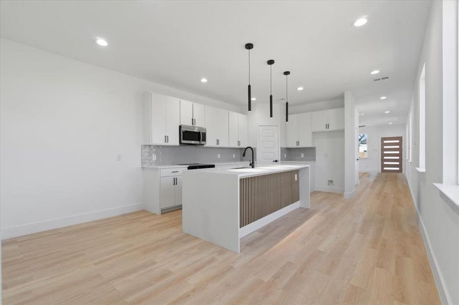 Kitchen featuring stainless steel microwave, decorative backsplash, white cabinets, a sink, and an island with sink