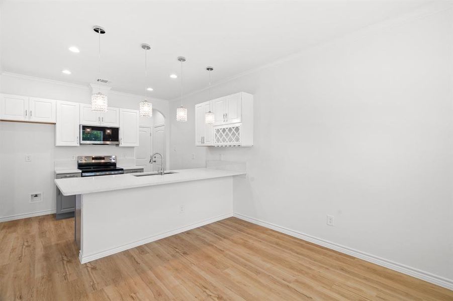 Kitchen with stainless steel appliances, a peninsula, white cabinets, light countertops, and ornamental molding Kitchen with stainless steel appliances, a peninsula, white cabinets, light countertops, and ornamental molding