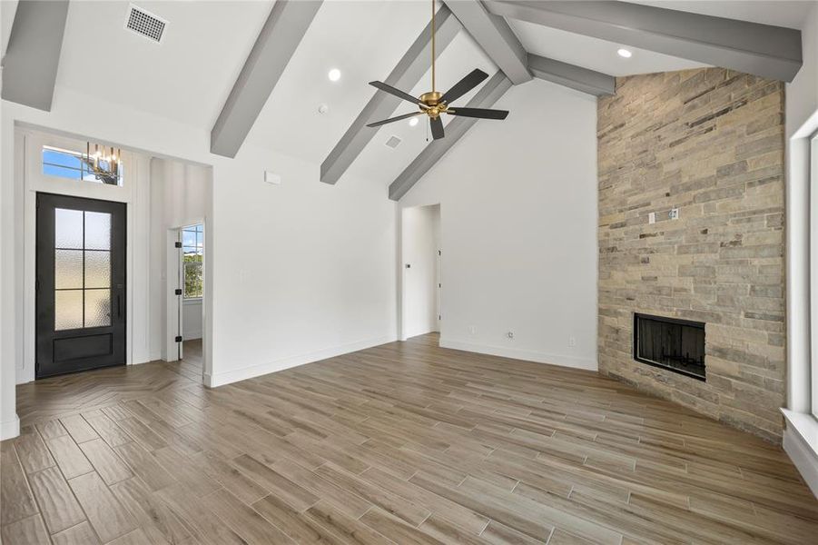 Unfurnished living room with high vaulted ceiling, beamed ceiling, a stone fireplace, light wood-type flooring, and a chandelier