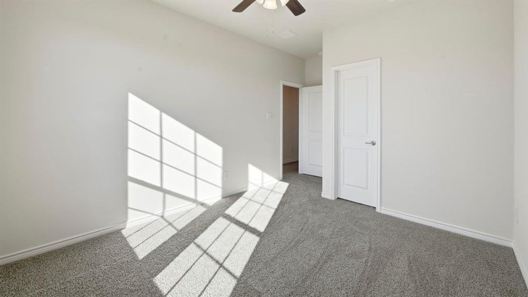 Spacious room featuring neutral walls, gray carpet flooring, white trim, and a ceiling fan