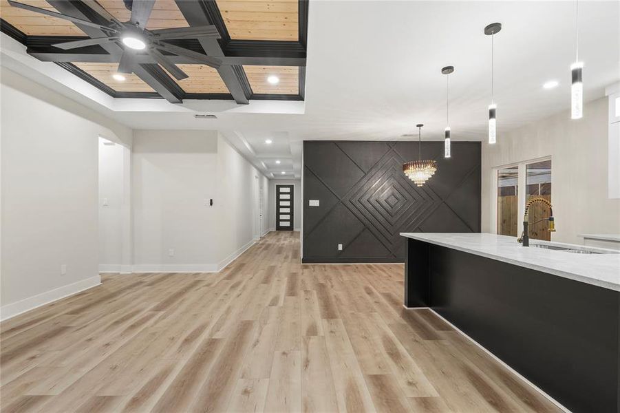 Unfurnished living room featuring coffered ceiling, a wooden ceiling with exposed beams, light wood-style flooring, an accent wall, and a chandelier