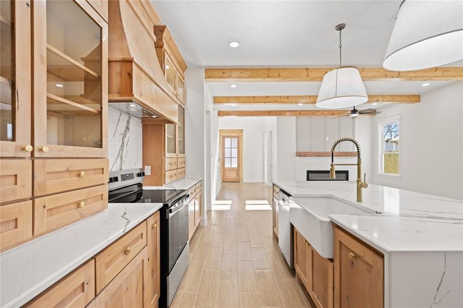 Kitchen with stainless steel appliances, light stone counters, pendant lighting, glass fronted cabinets, and beam ceiling Kitchen with stainless steel appliances, light stone counters, pendant lighting, glass fronted cabinets, and beam ceiling