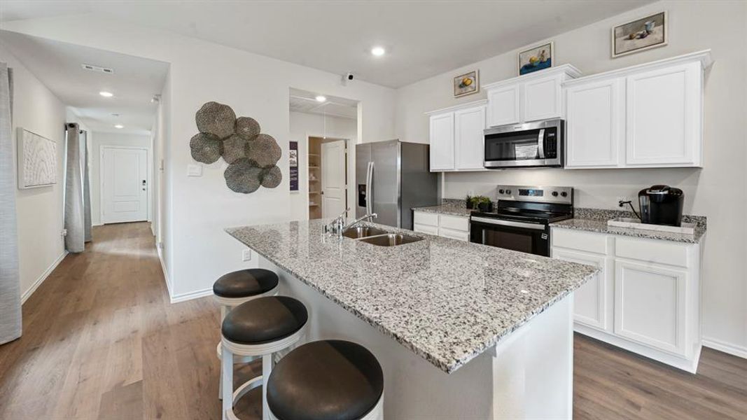 Kitchen featuring appliances with stainless steel finishes, white cabinets, a breakfast bar area, light stone counters, and recessed lighting Kitchen featuring appliances with stainless steel finishes, white cabinets, a breakfast bar area, light stone counters, and recessed lighting