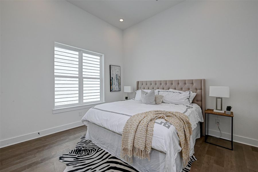 The spacious primary bedroom features soaring ceilings, hardwood floors, and abundant natural light filtered through designer window treatments the perfect retreat.