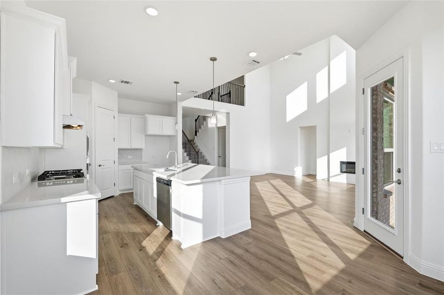 Kitchen featuring white cabinets, light wood-style floors, decorative light fixtures, a kitchen island with sink, and open floor plan Kitchen featuring white cabinets, light wood-style floors, decorative light fixtures, a kitchen island with sink, and open floor plan
