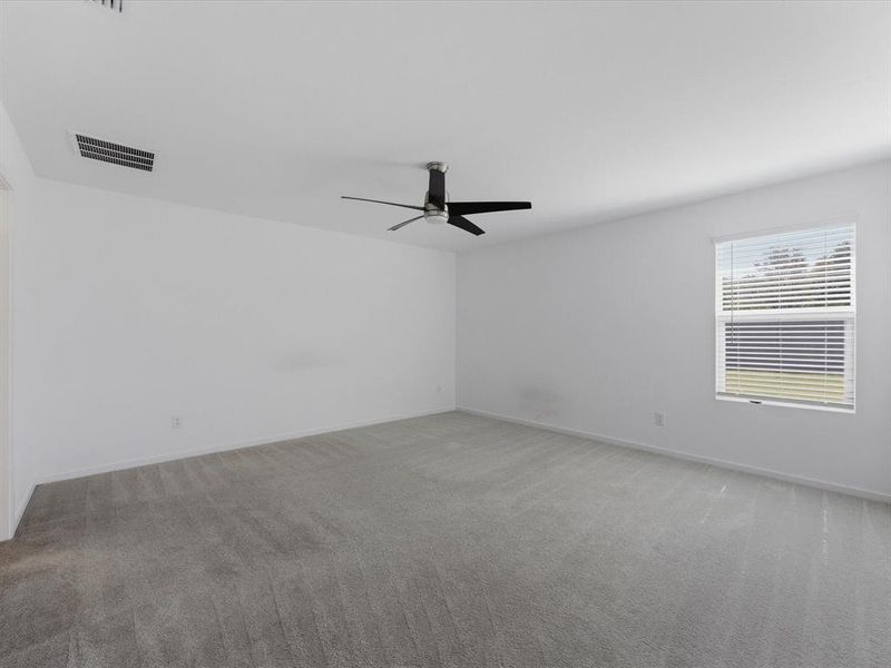 Spacious room featuring light gray carpeting, a contemporary ceiling fan with black blades, and a window with horizontal blinds
