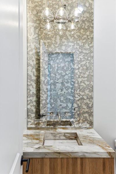 Located off the foyer, the main floor powder room features a custom floating vanity with ribbed white oak detail and a full-height antique mirror. The quartz countertops are paired with a wall-mounted designer chrome faucet and an under-mount white sink. The space is elegantly illuminated by three globe designer sconces, and it includes engineered white oak flooring and a Toto commode.