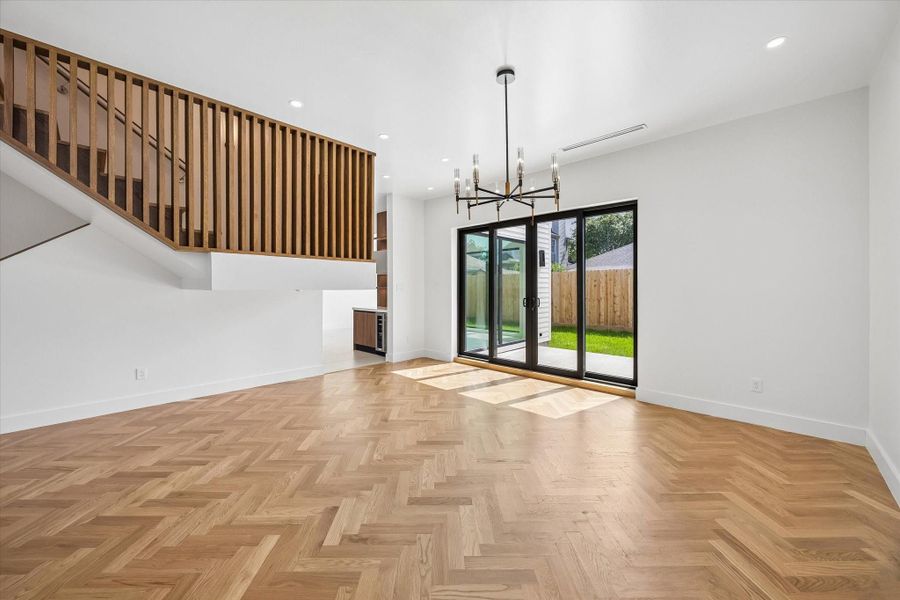 Bright and modern living area featuring elegant herringbone wood floors, a stylish chandelier, and large sliding glass doors opening to a private backyard. Bright and modern living area featuring elegant herringbone wood floors, a stylish chandelier, and large sliding glass doors opening to a private backyard.