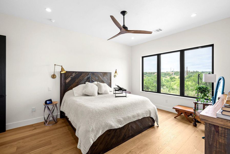 Warm hardwood flooring and large windows frame serene treetop views in this inviting bedroom.