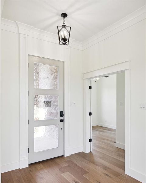 Foyer entrance featuring light wood-type flooring, crown molding, and an inviting chandelier