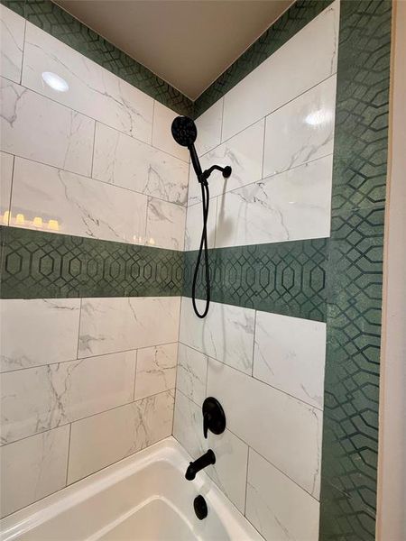 Bathtub and shower combination featuring white marble-look subway tile and a decorative green geometric tile accent band Bathtub and shower combination featuring white marble-look subway tile and a decorative green geometric tile accent band