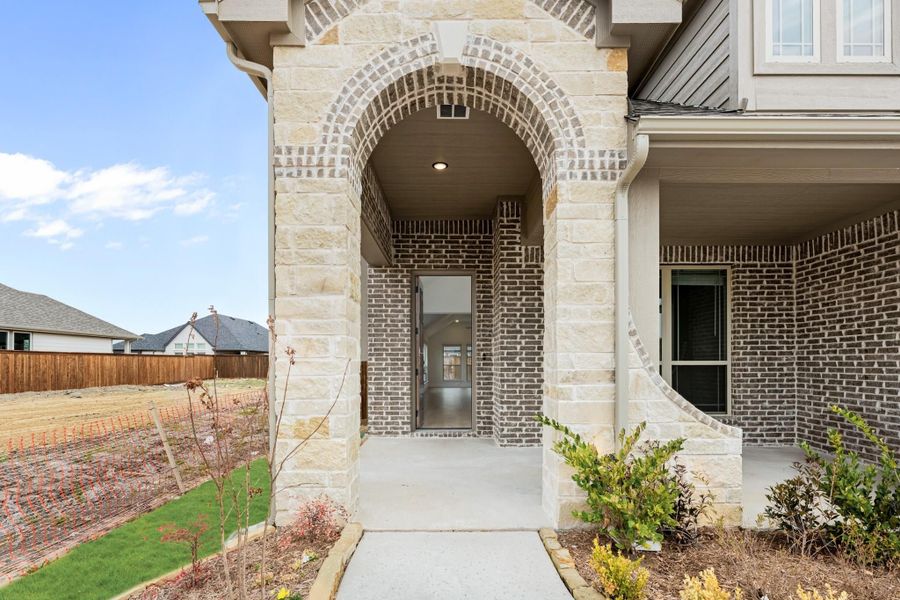 Home entrance with stone arch, brick exterior, covered porch, and concrete walkway leading to front door Home entrance with stone arch, brick exterior, covered porch, and concrete walkway leading to front door