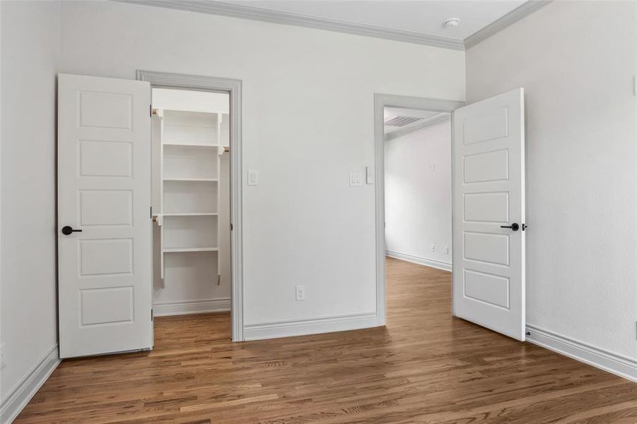 Bedroom featuring ornamental molding, a spacious closet, and wood finished floors Bedroom featuring ornamental molding, a spacious closet, and wood finished floors