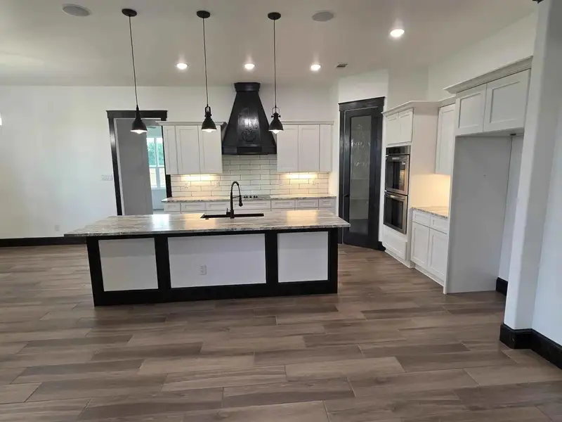 Kitchen with white cabinets, a center island with sink, decorative light fixtures, dark wood-style flooring, and light stone counters Kitchen with white cabinets, a center island with sink, decorative light fixtures, dark wood-style flooring, and light stone counters