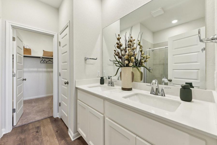 Double vanities with clean white countertops sit adjacent to a spacious walk-in closet.