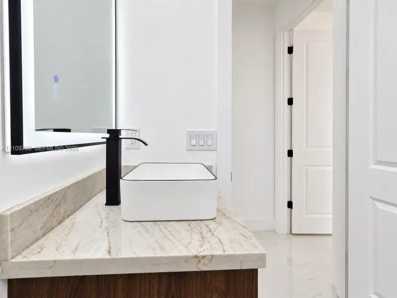 Stone countertop vanity featuring a rectangular vessel sink, matte black tall-spout faucet, and a wall-mounted LED-backlit mirror