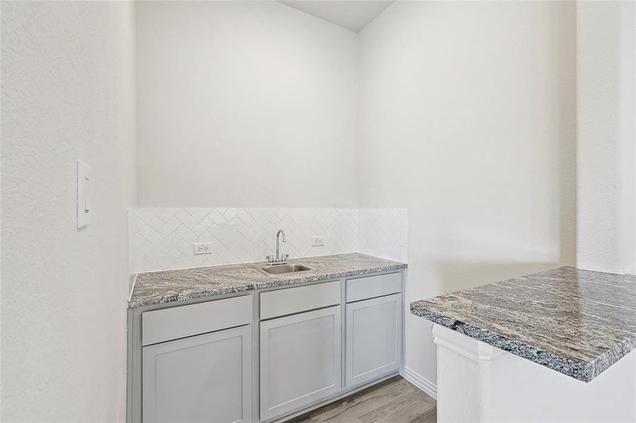 Kitchen featuring light wood-type flooring, backsplash, stone countertops, sink, and gray cabinetry