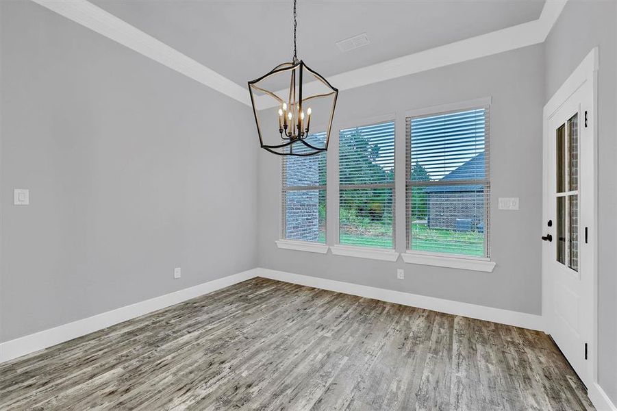 Unfurnished room featuring an inviting chandelier, wood-type flooring, and crown molding