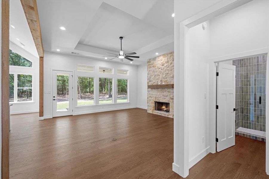 living room with a ceiling fan, dark wood-style flooring, a raised ceiling, a stone fireplace, and recessed lighting living room with a ceiling fan, dark wood-style flooring, a raised ceiling, a stone fireplace, and recessed lighting