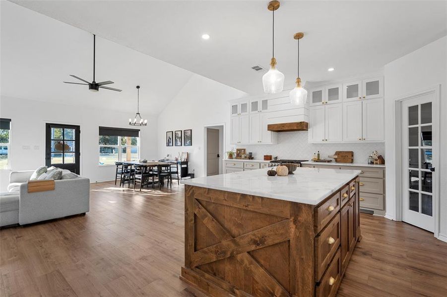Kitchen with hanging light fixtures, open floor plan, glass insert cabinets, decorative backsplash, and high vaulted ceiling