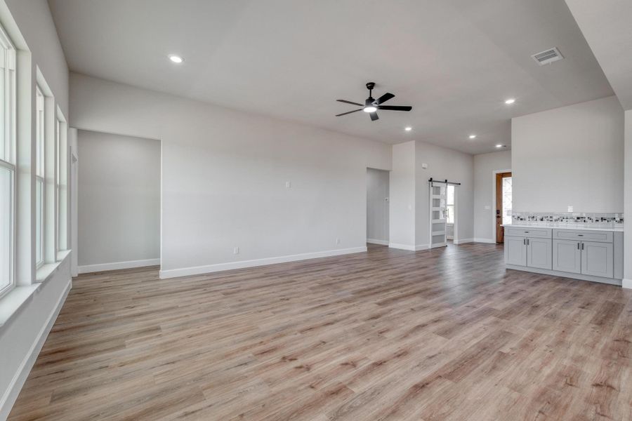 Unfurnished living room with ceiling fan, a barn door, light wood-style floors, recessed lighting, and baseboards