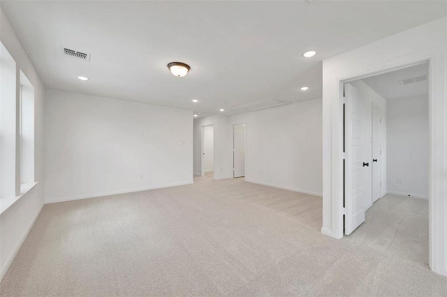 Spacious room featuring light-toned carpeting, multiple recessed lights, and white paneled doors with dark hardware
