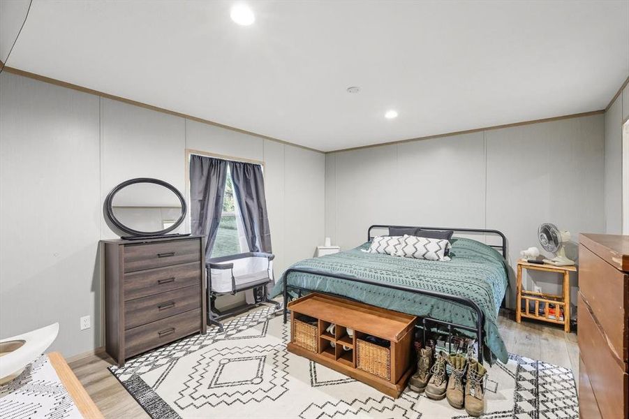 Bedroom with light wood-type flooring, ornamental molding, recessed lighting, and a decorative wall Bedroom with light wood-type flooring, ornamental molding, recessed lighting, and a decorative wall