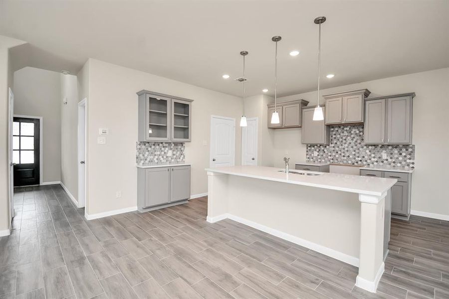 The warm tones of the wood cabinetry of this kitchen creates a cozy feel, while the stainless steel appliances and pendant lights add a touch of modern elegance. *This image is from another Saratoga Home with similar floor plan and finishes, not the Brittany floorplan.*