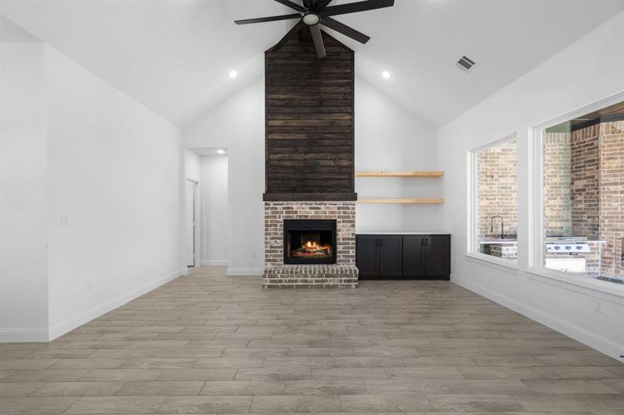 Unfurnished living room with ceiling fan, high vaulted ceiling, a fireplace, and light hardwood / wood-style floors