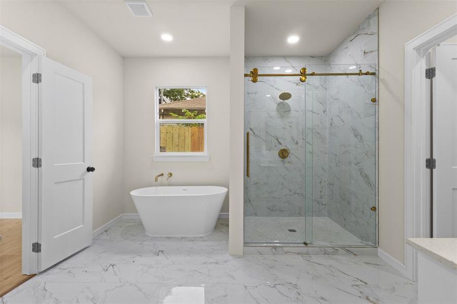 Bathroom featuring a freestanding soaking tub with gold-tone fixtures, a glass-enclosed shower with gold-tone hardware and marble-patterned tile, and large format marble-patterned floor tiles