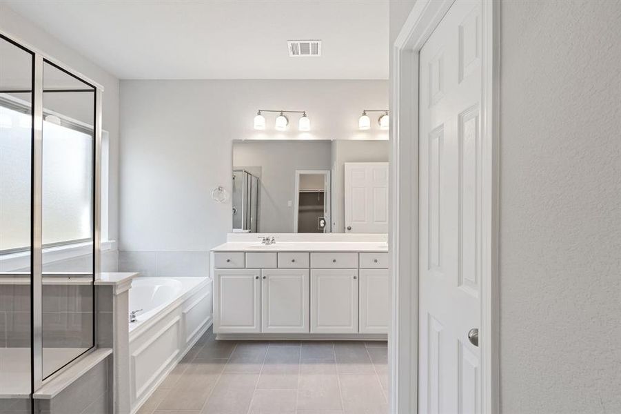 This additional view of your primary bathroom features tile flooring, fresh paint, walk-in shower, a separate garden tub, and a large walk-in closet.